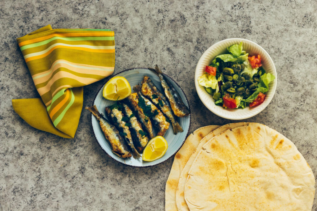 fried sardines on the plate decorated with lemon and parsley, algerian salad and beans, tomato in bowl