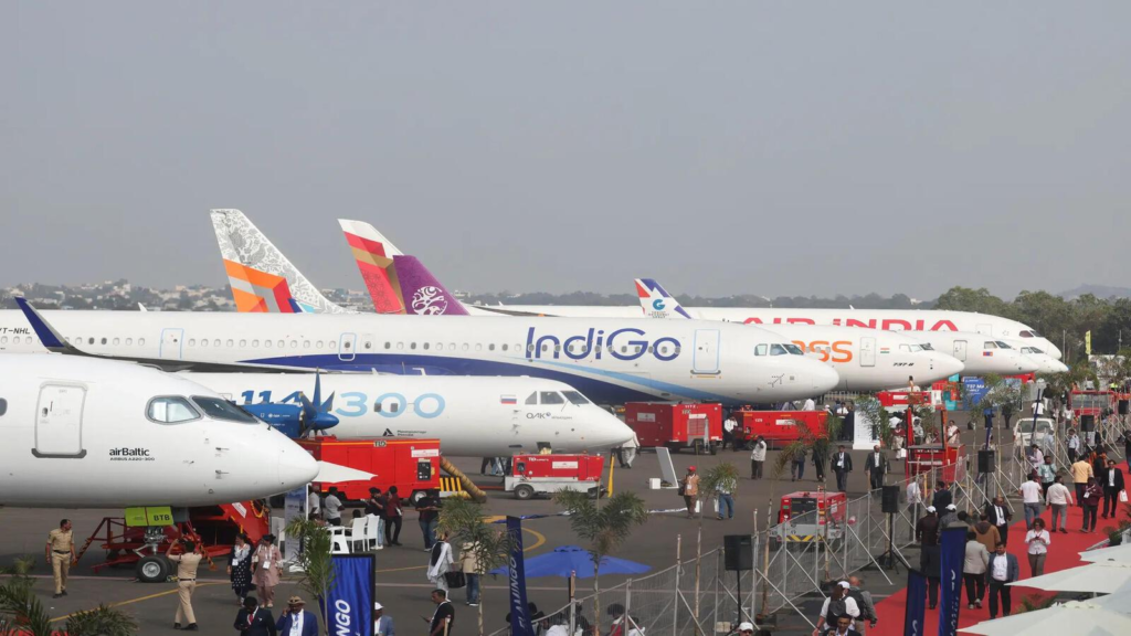 An IndiGo aircraft parked in a line with planes from Air India, Akasa Air, and airBaltic at an airfield