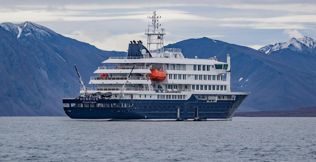 MV Hondius expedition cruise ship at sea with snow-dusted mountains in the background