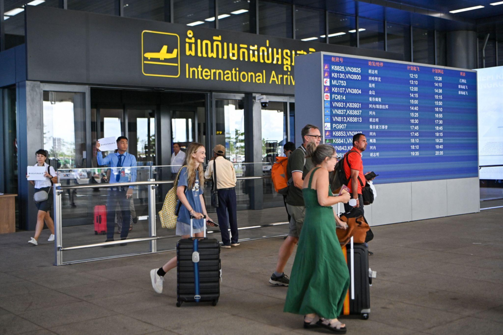 Travelers with luggage exit an International Arrivals gate past people holding pickup signs