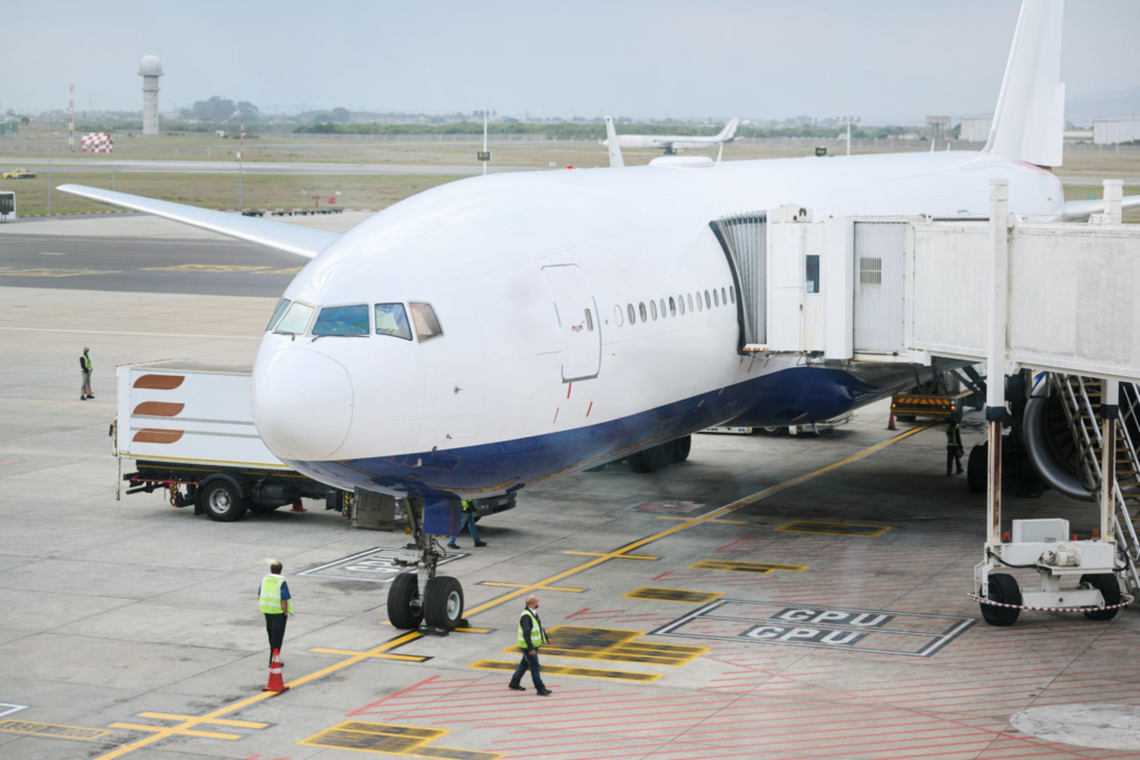 A large passenger jet parked at an airport gate with a jet bridge attached and ground crew on the tarmac