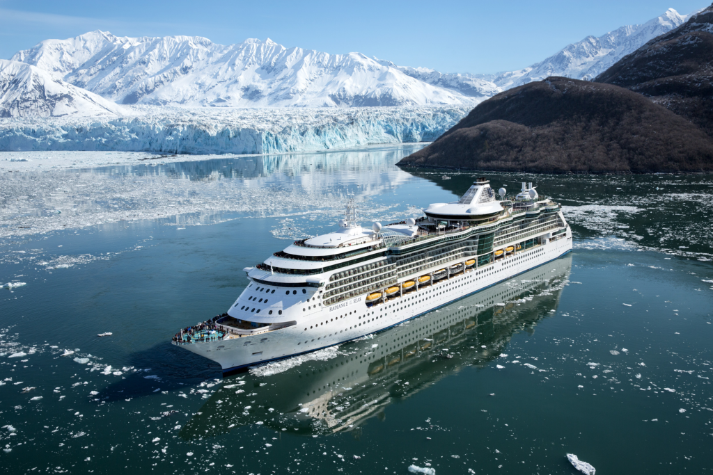 A cruise ship navigating ice-filled waters in front of a massive glacier and snow-covered mountains