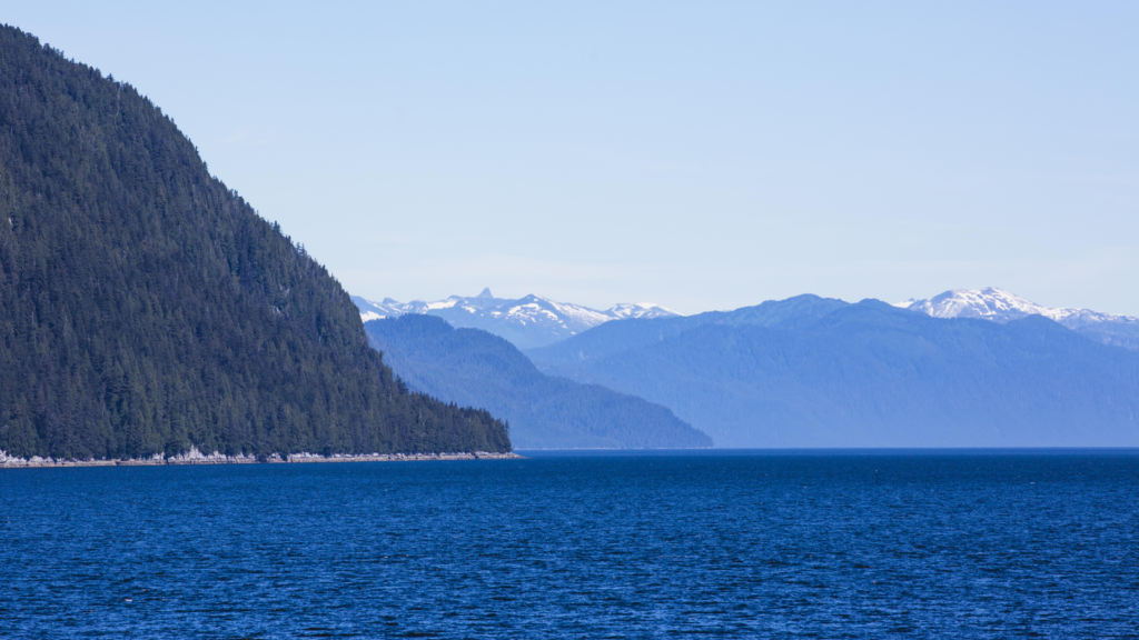 Forested mountains and snow-capped peaks along a deep blue coastal waterway