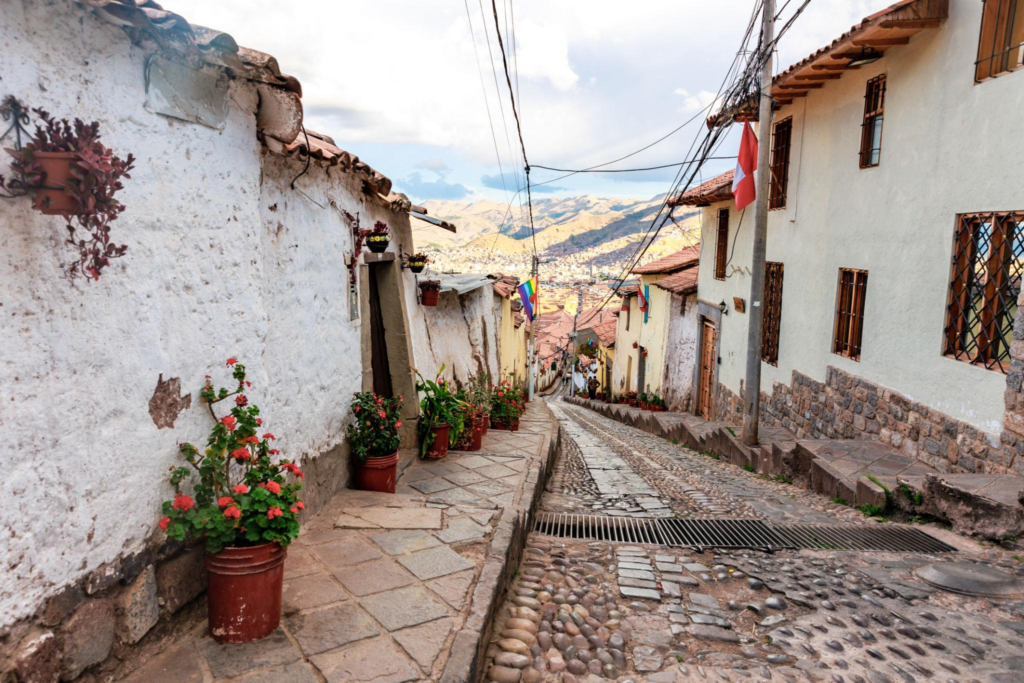 Narrow, steep cobblestone street in Cusco with white-washed buildings and a view of the city and mountains