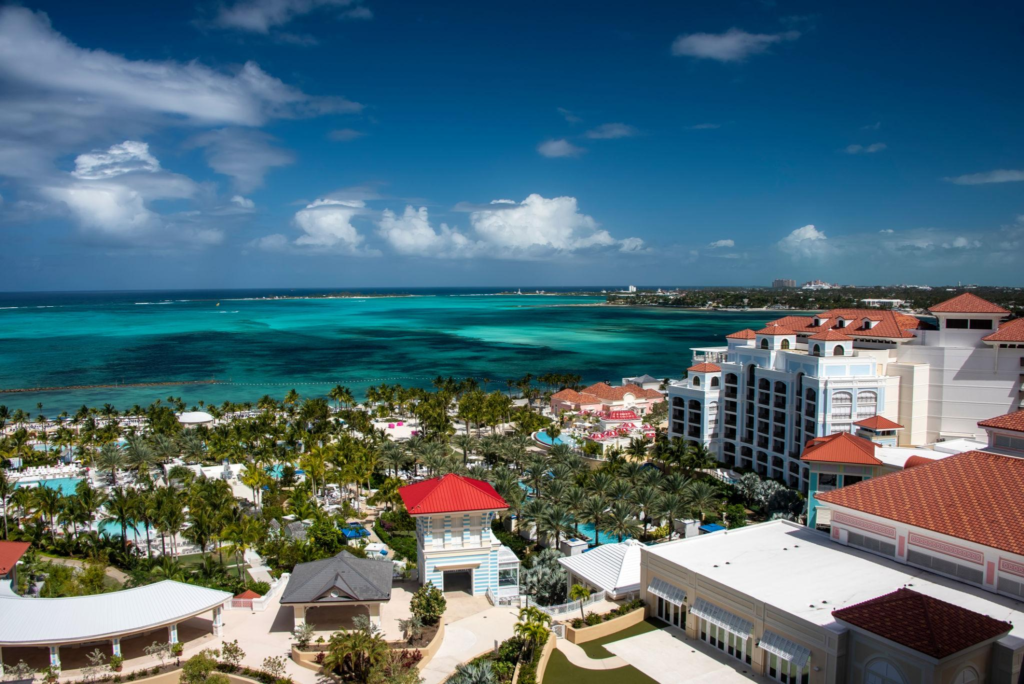 Aerial view of a sprawling resort in The Bahamas with red-roofed buildings, palm trees, and turquoise ocean