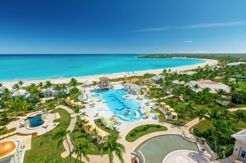 Aerial view of a Sandals resort with a large pool, palm trees, and a white sand beach along turquoise water