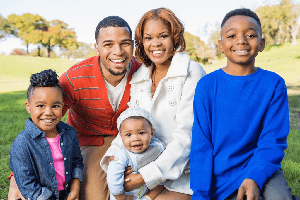 A smiling Black family of five with three children outdoors in a grassy park